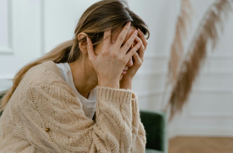 A woman sitting indoors covering her face in frustration, depicting stress and mental health challenges.